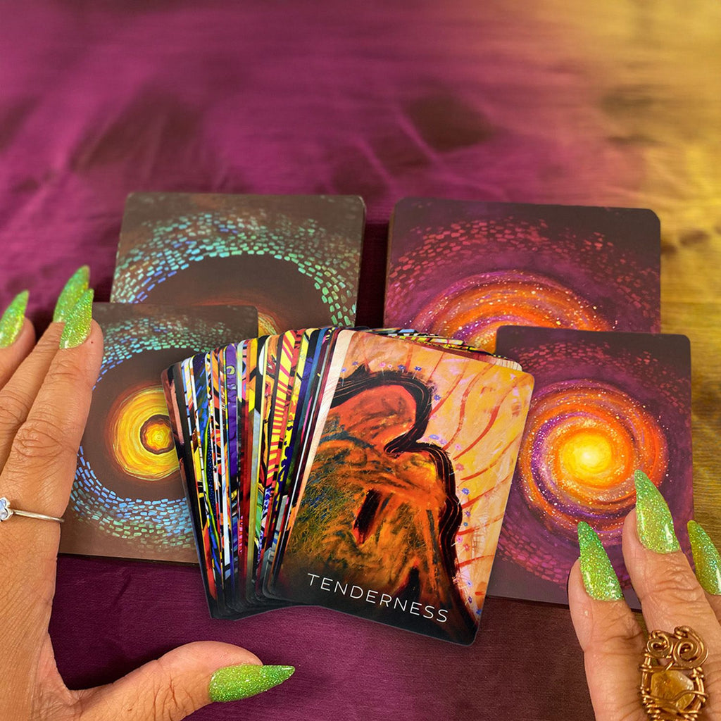 Black Woman's hands holding Wisdom of the Shadow and Wisdom of the Divine Feminine Oracle cards with a colorful and mystical design on a purple surface.