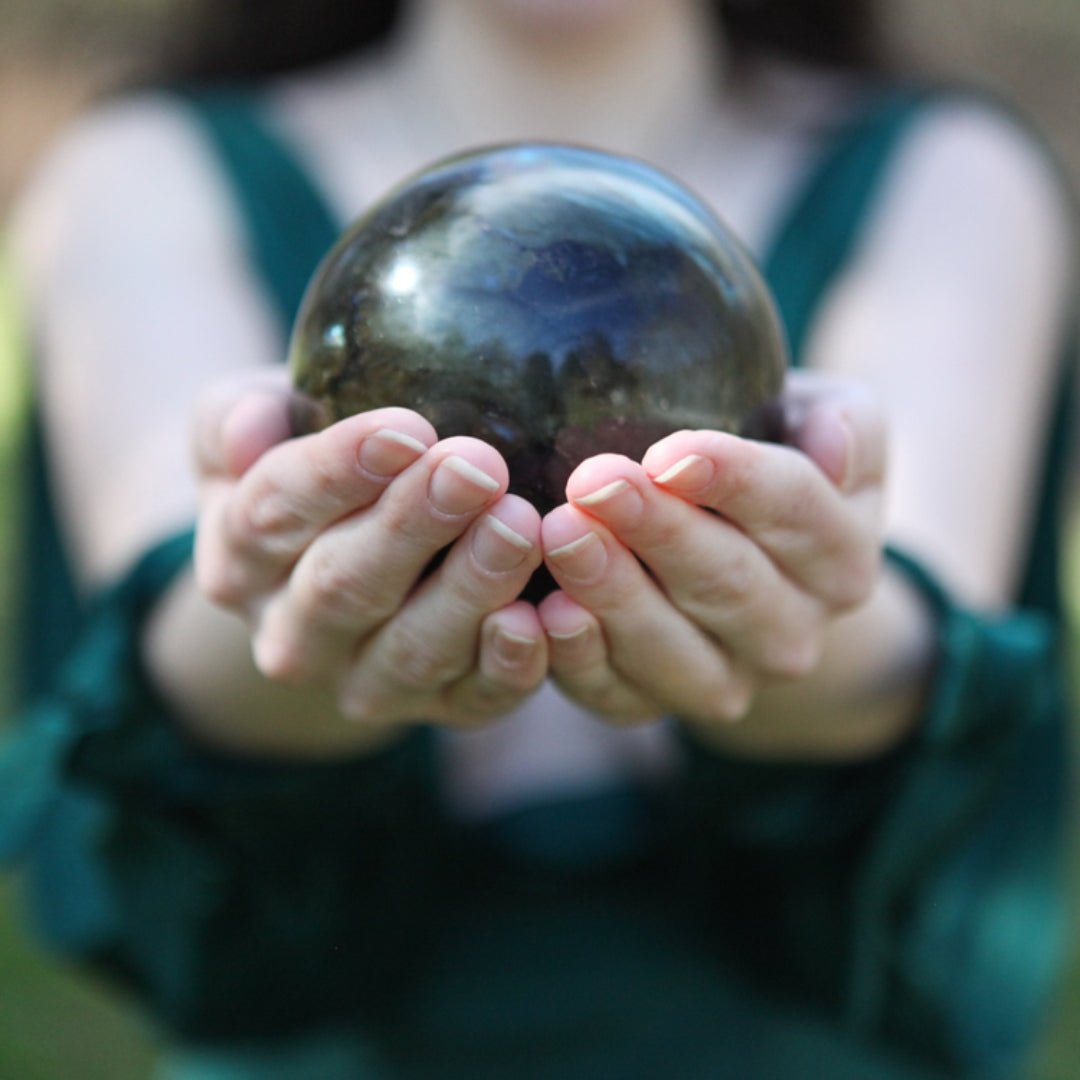 Priestess, Author, and Ritualist Jessica Ricchetti holding a large labradorite sphere in the palm of her outstretched hands.